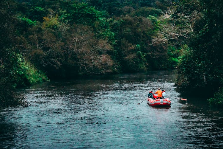 Three Persons Riding Red Inflatable Raft