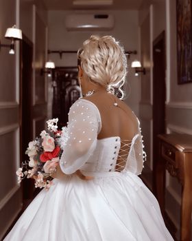 A bride showcasing a beautiful wedding dress and bouquet while walking through an elegant indoor corridor.