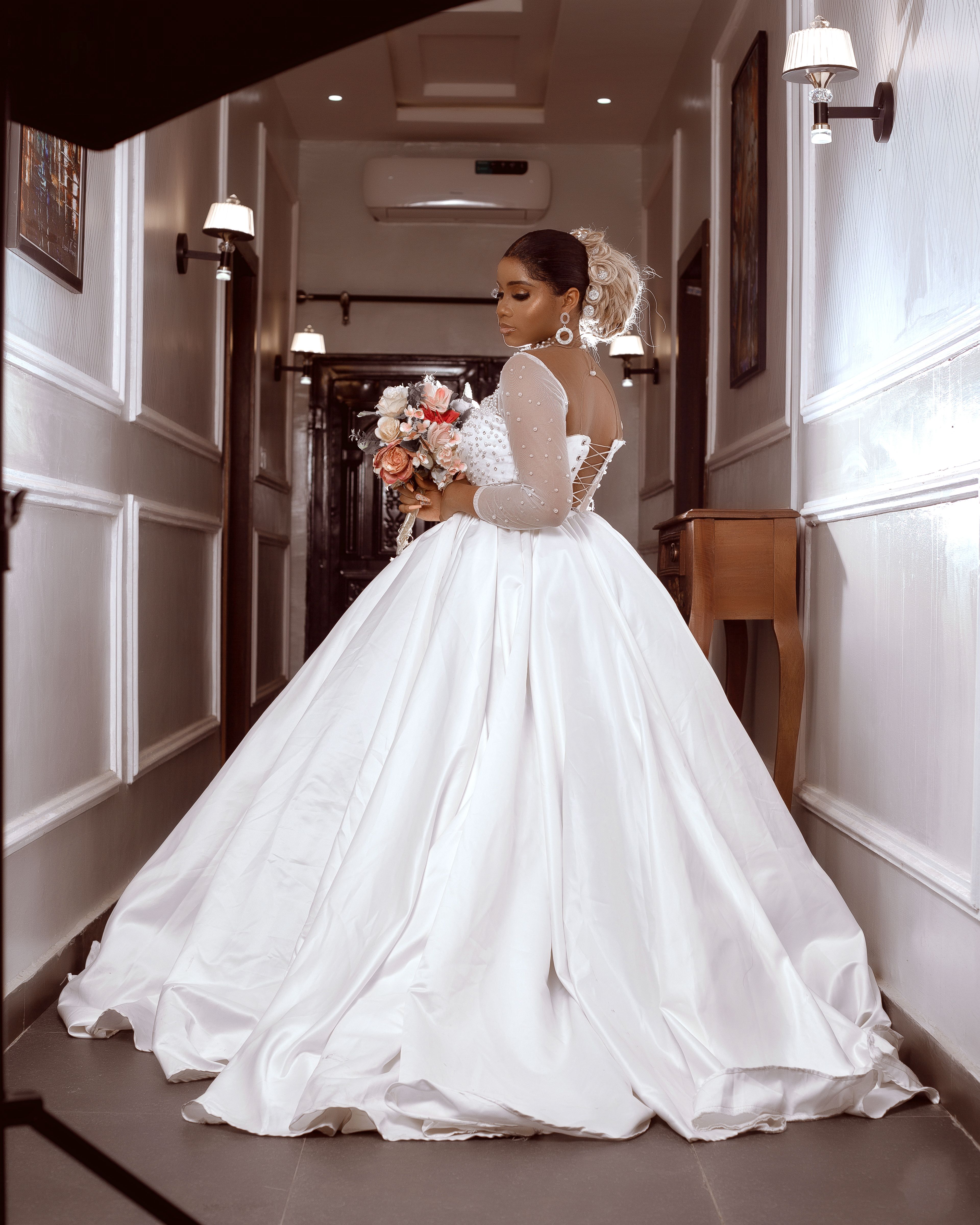 Stunning bride in elegant white wedding dress holding bouquet indoors.
