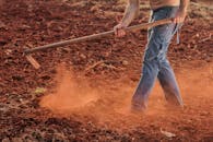 赤脚农民穿着牛仔裤，在乡村的红土地上用锄头耕种