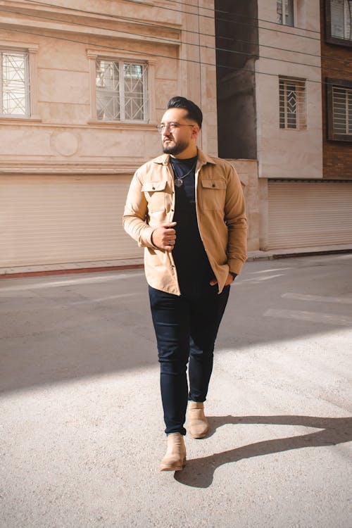 A man in a tan jacket and jeans walking down the street