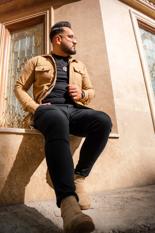 A man sitting on a ledge in a tan jacket