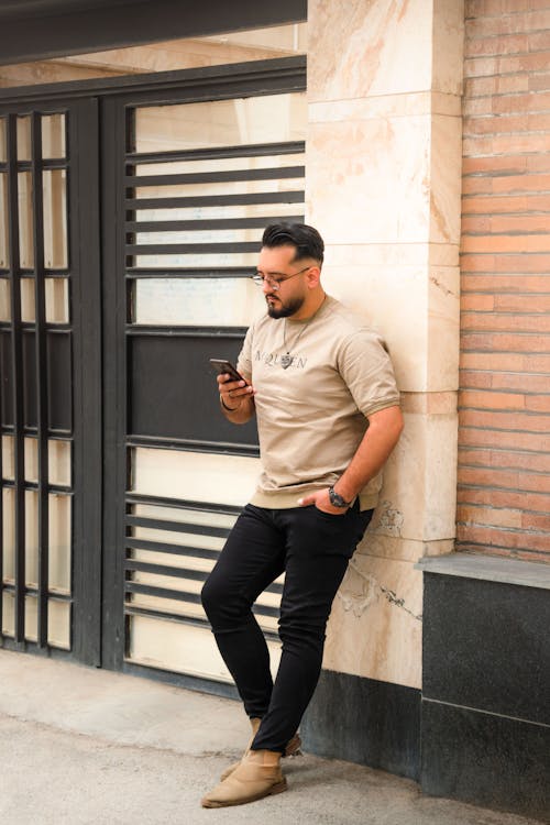 A man in a tan shirt and black pants is looking at his cell phone