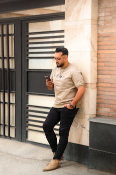 Adult man casually leaning on an urban wall, checking his smartphone.