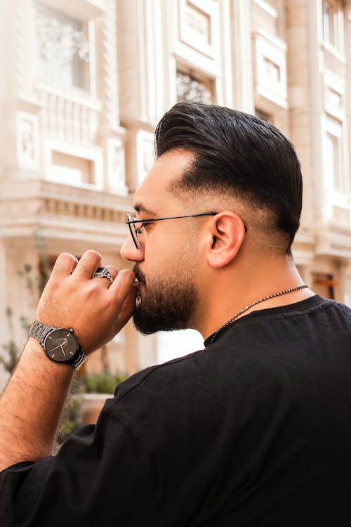 A man with glasses and a beard is smoking a cigarette