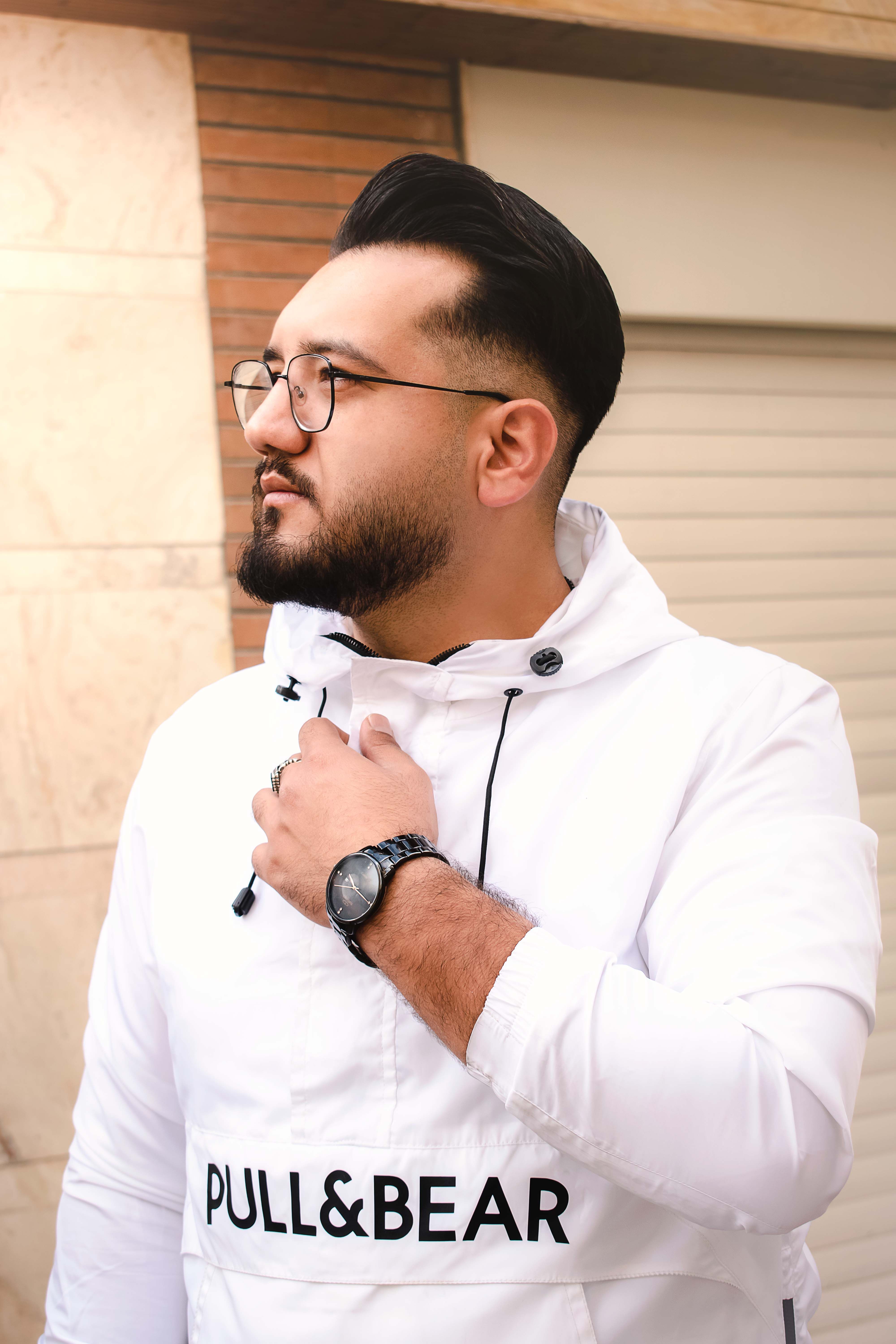 Young man in a white Pull&Bear jacket with glasses, looking sideways outdoors.