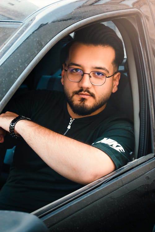 A man with glasses and a beard sitting in a car