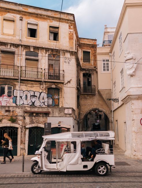 Charming street view in Lisbon featuring a tuk-tuk, historic buildings, and urban graffiti.
