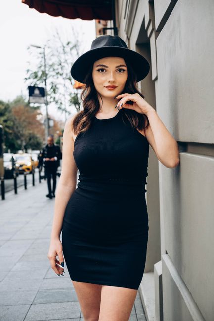 Fashionable woman in a bodycon dress with a black fedora standing stylishly on a city street in Turkey.