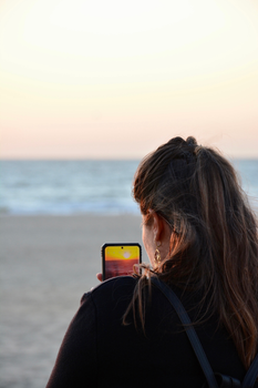 A woman captures the serene sunset at Ostende beach using her smartphone, creating lasting memories.