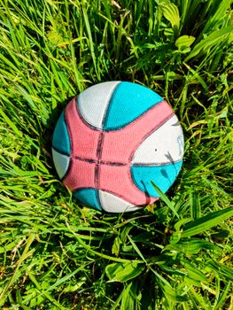 Vibrant multicolored basketball resting on a lush, sunlit grass lawn, perfect for summer recreation.