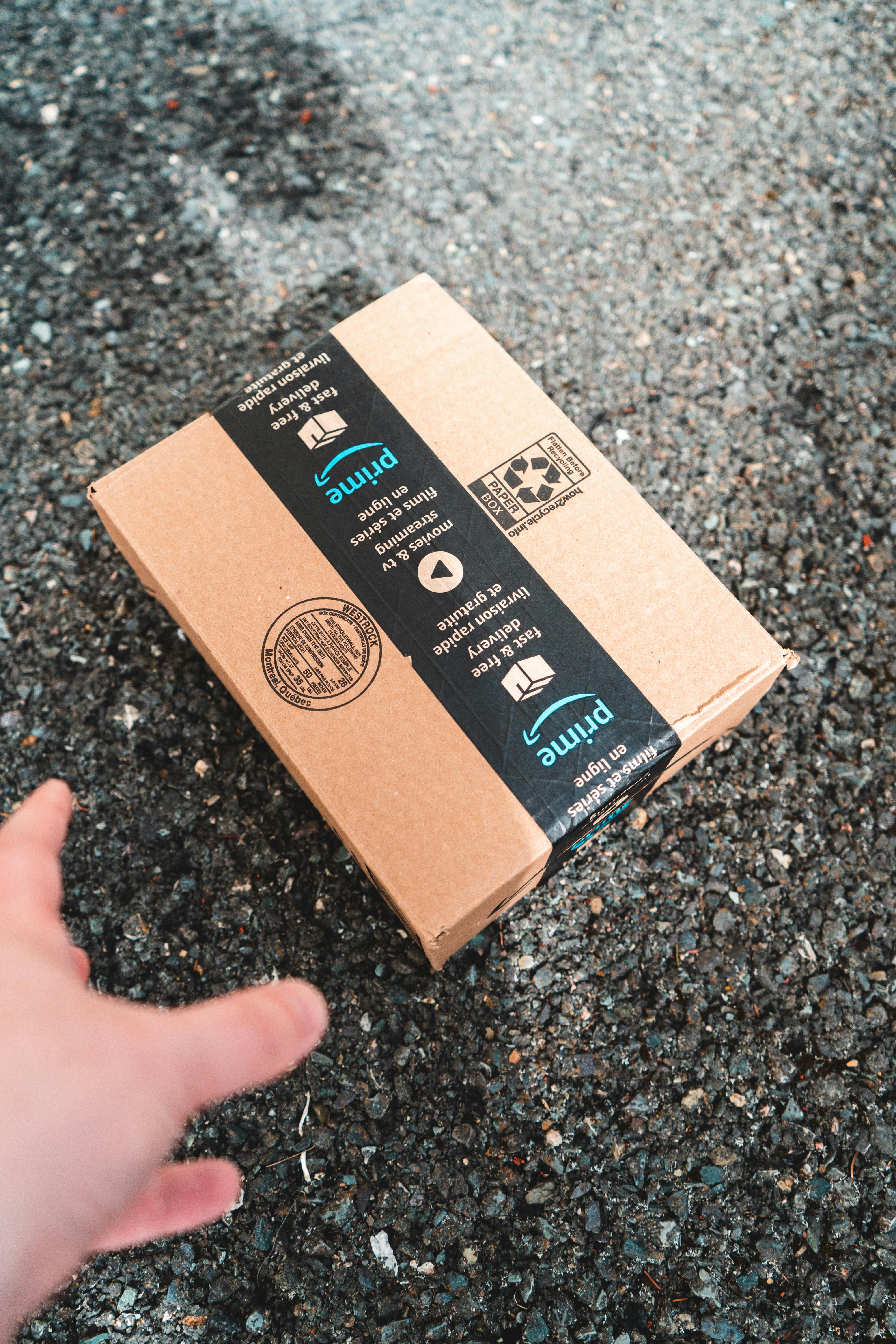 Hand reaching for a cardboard package on a gravel surface, suggesting online delivery.