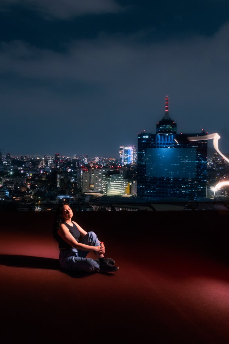 Woman Sitting On Rooftop In City Downtown At Night