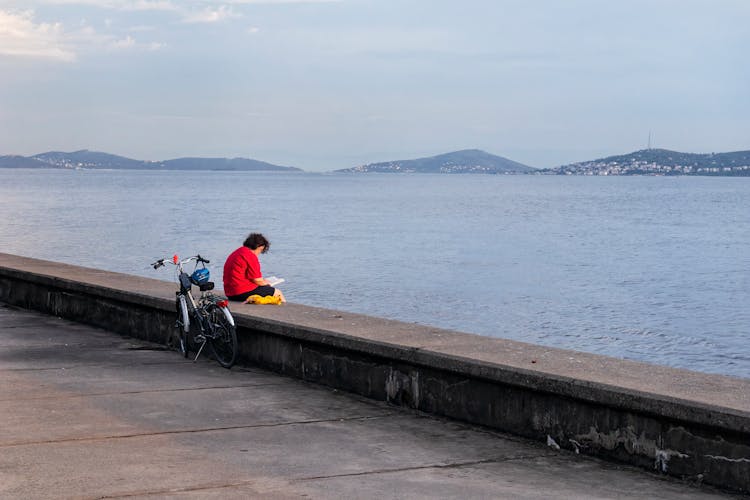 Woman Reading A Book Sitting On The Edge Of The Pier