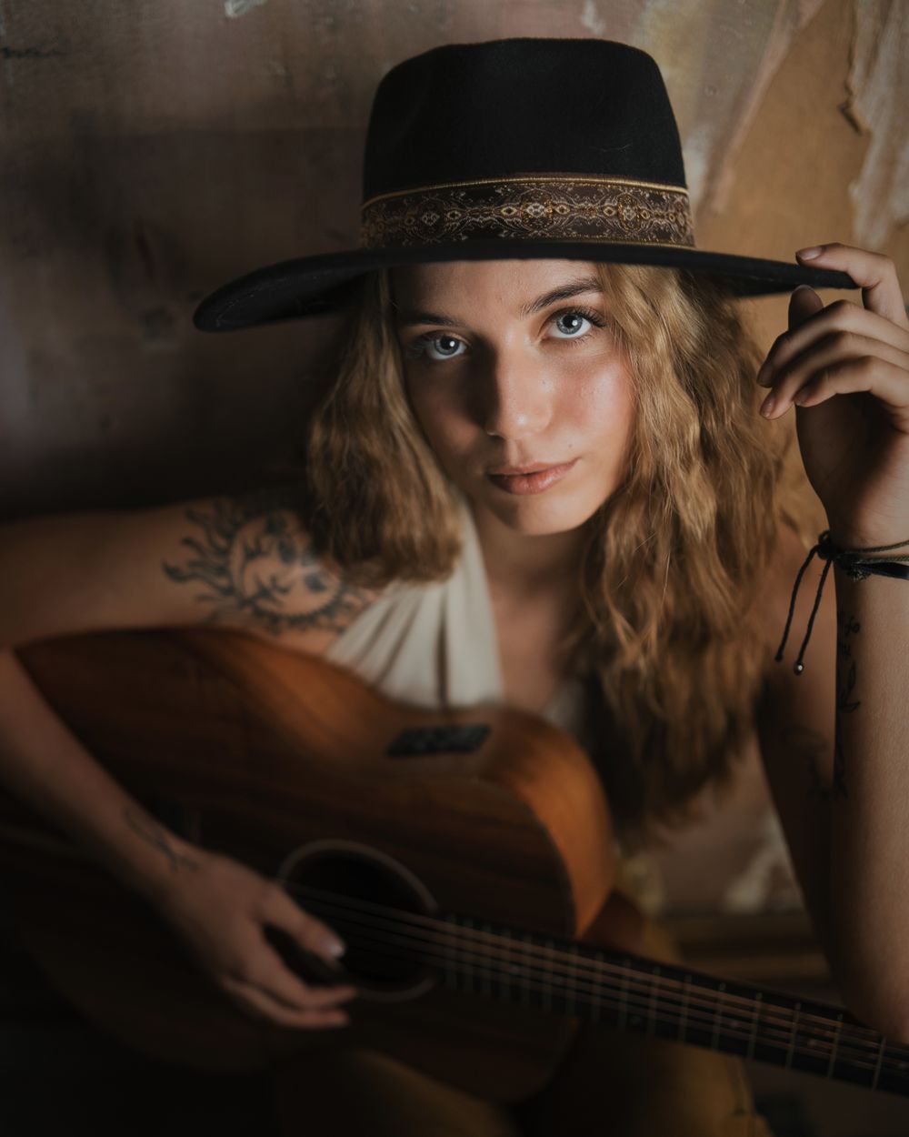 Songwriter in a wide-brimmed hat holding an acoustic guitar in low light — photo by Chris S on Pexels