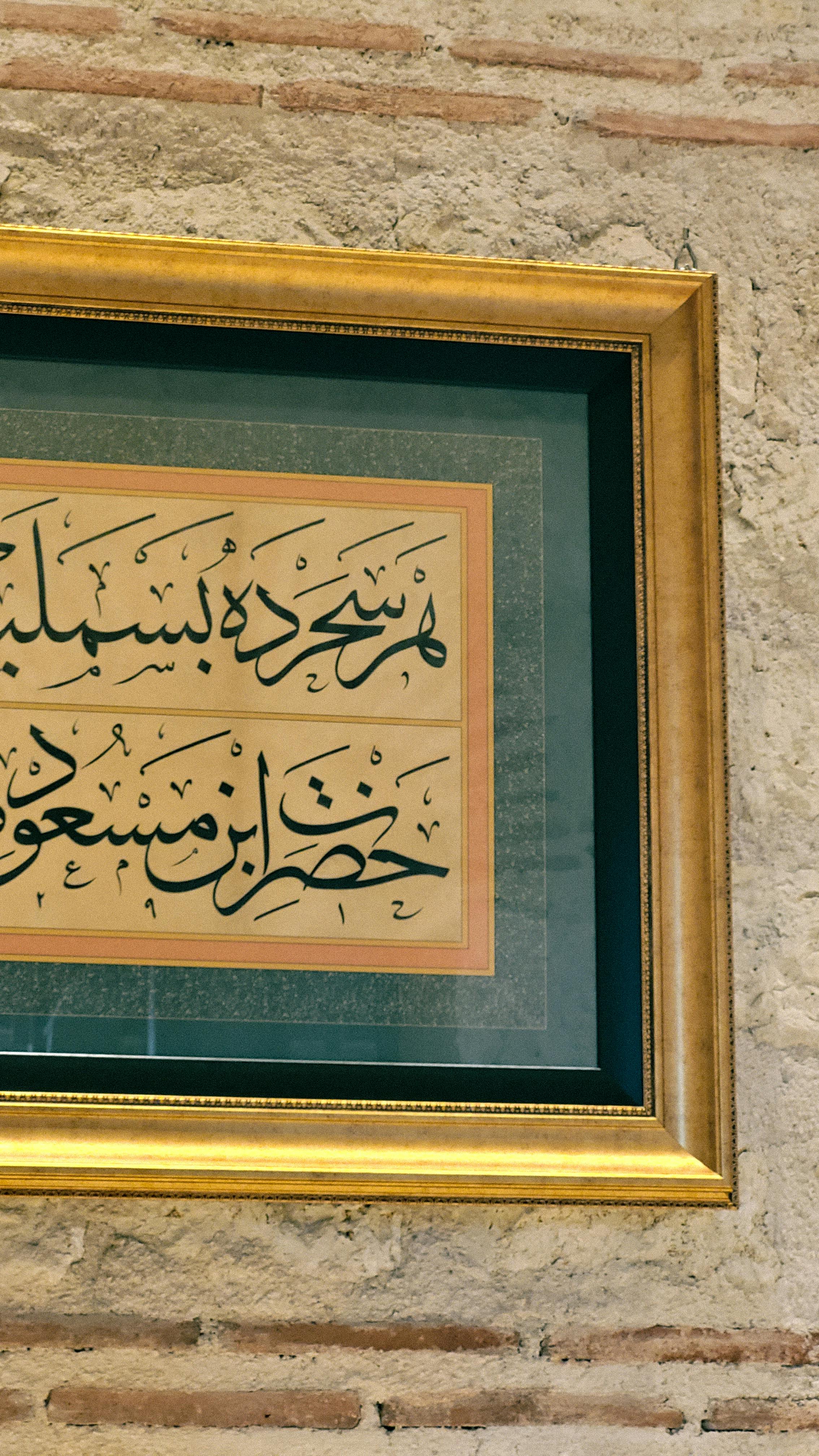 Close-up of framed Arabic calligraphy on a textured wall, showcasing intricate design and elegance.