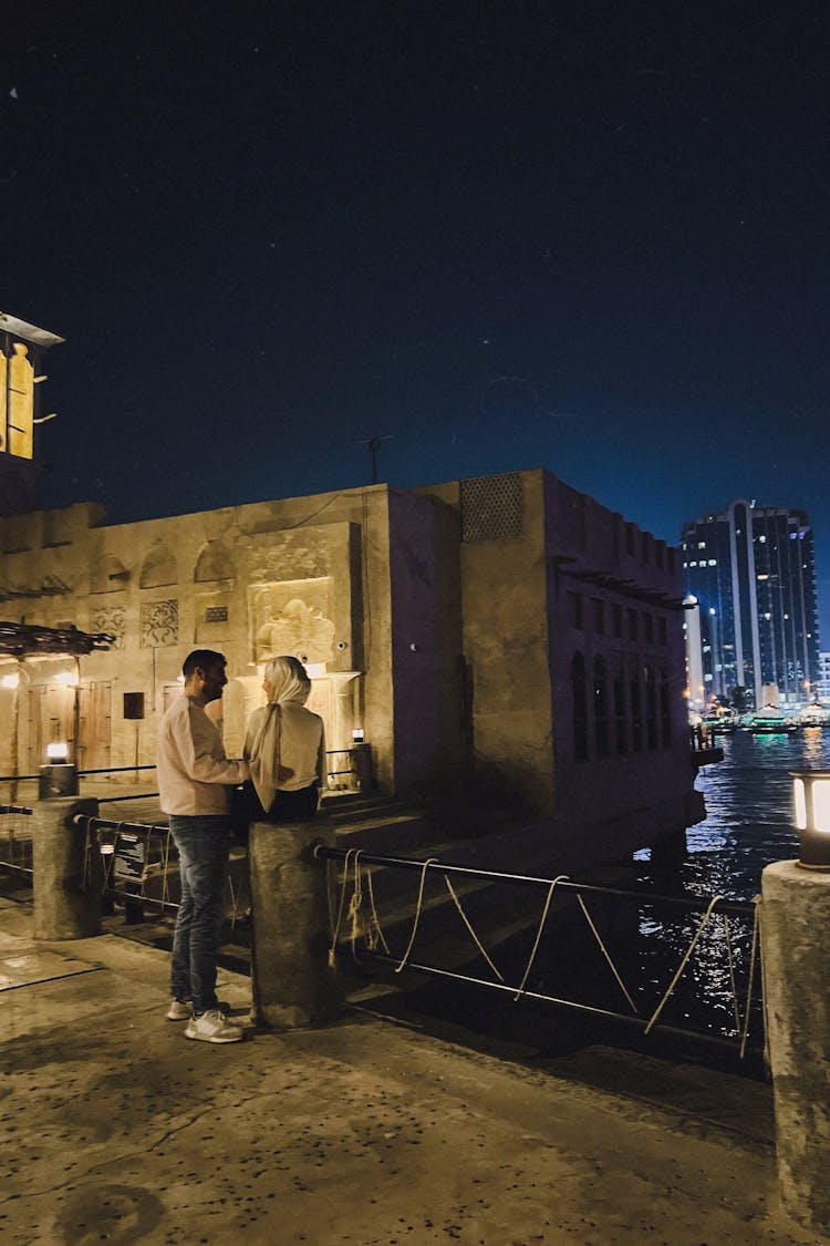 Couple Standing Near Water In City At Night