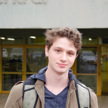 Casual portrait of a young man with a backpack standing outside a building.