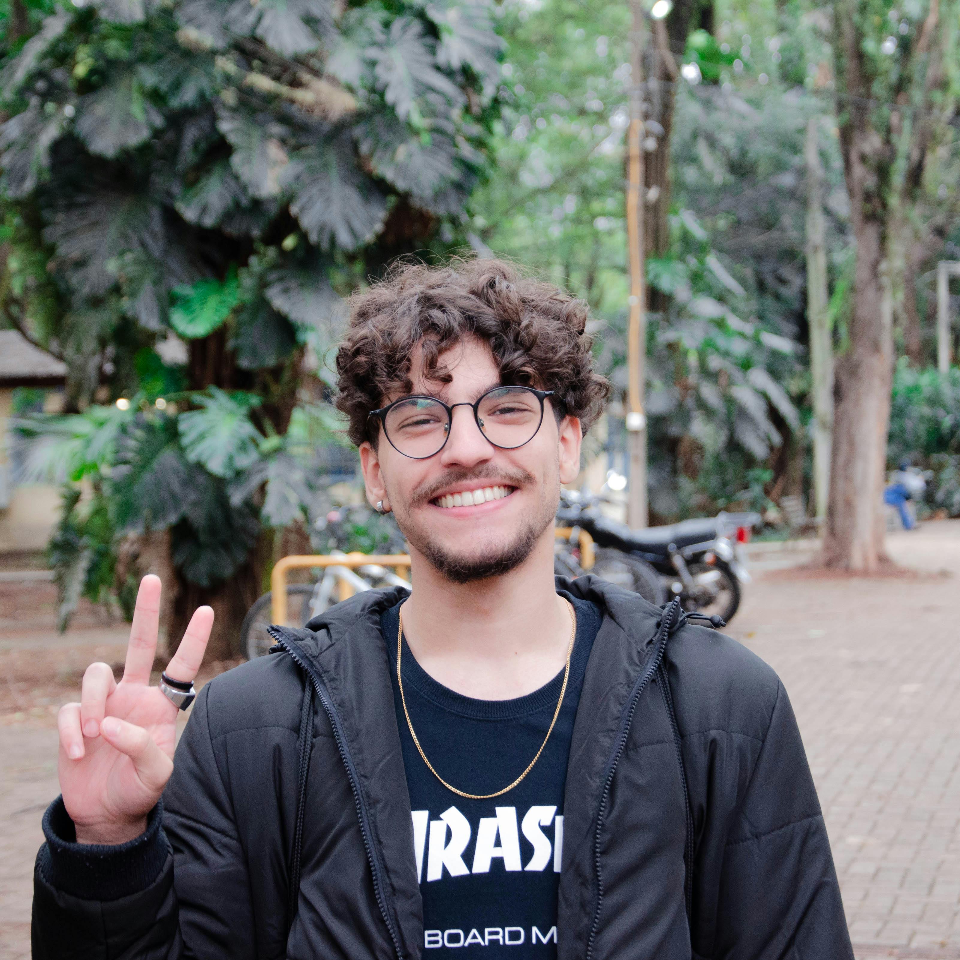 A young man smiling and posing with a peace sign in a park setting.
