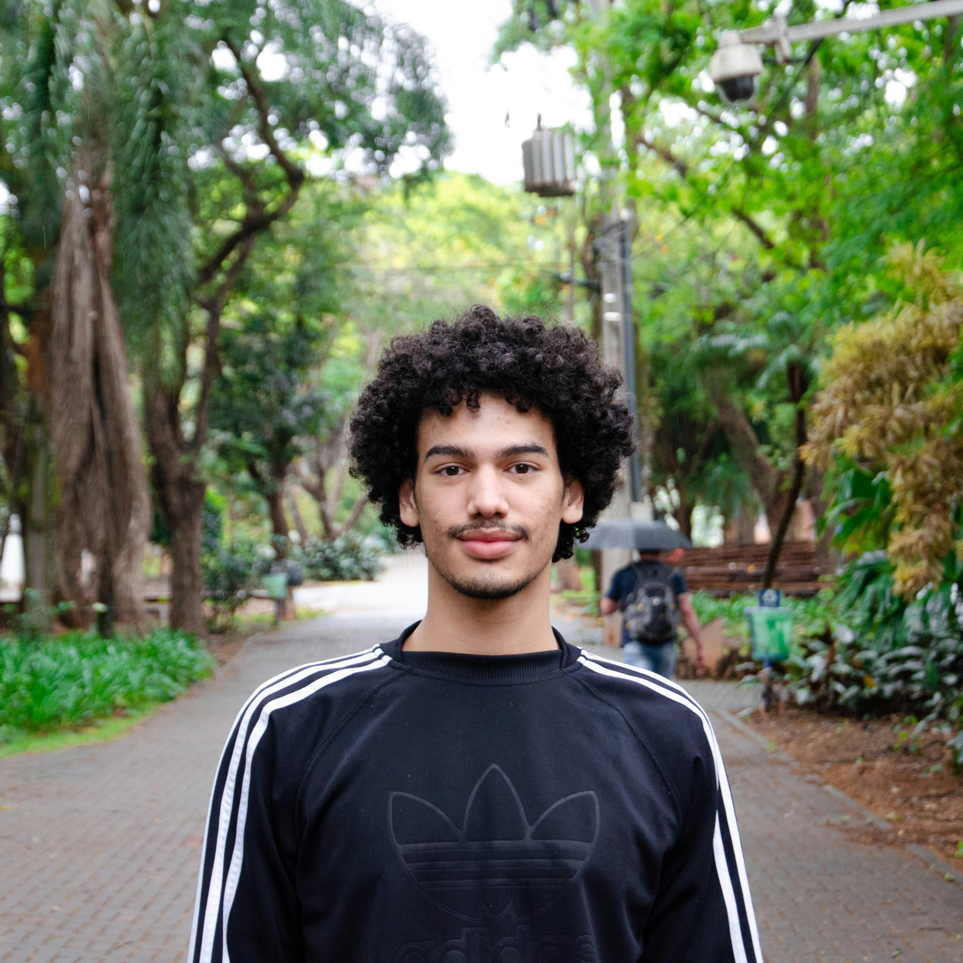Portrait of a young man with curly hair standing in a lush green park.