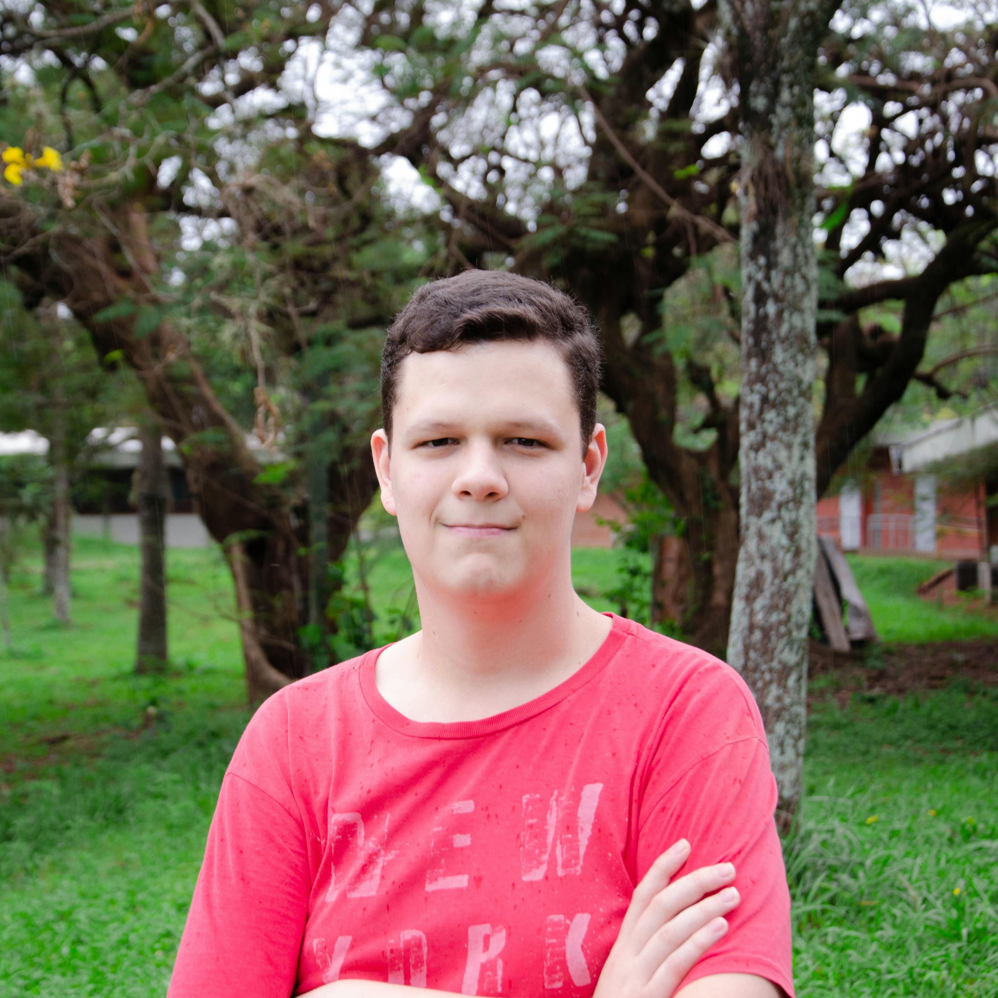 Portrait of a teenage boy standing with arms crossed in a lush garden setting.