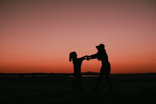 Silhouette of Mother and Daughter Holding Hands at Dusk on Red Sky