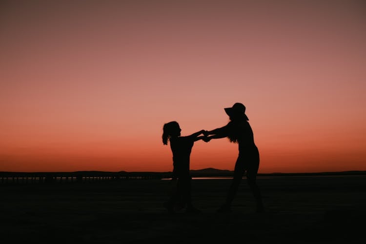 Silhouette Of Mother And Daughter Holding Hands At Dusk On Red Sky