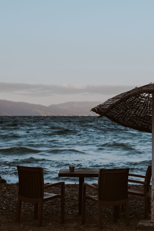 Free A peaceful seaside view with chairs, umbrellas, and gentle waves captured at sunset. Stock Photo