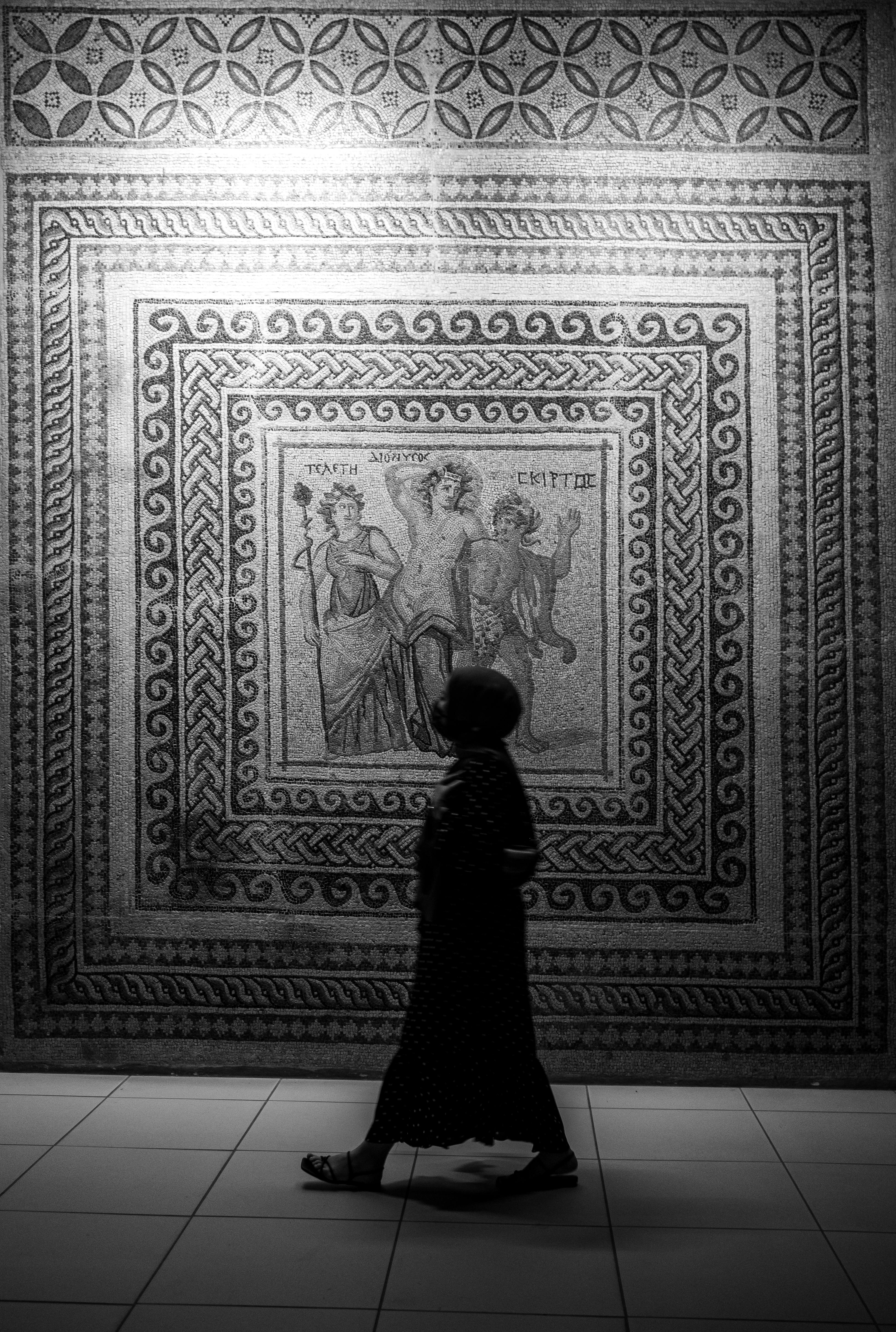 a woman walking in front of a wall with a mosaic