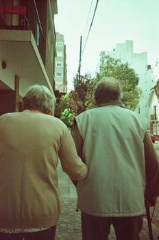 Senior couple walking hand in hand in an urban neighborhood, symbolizing togetherness in retirement.