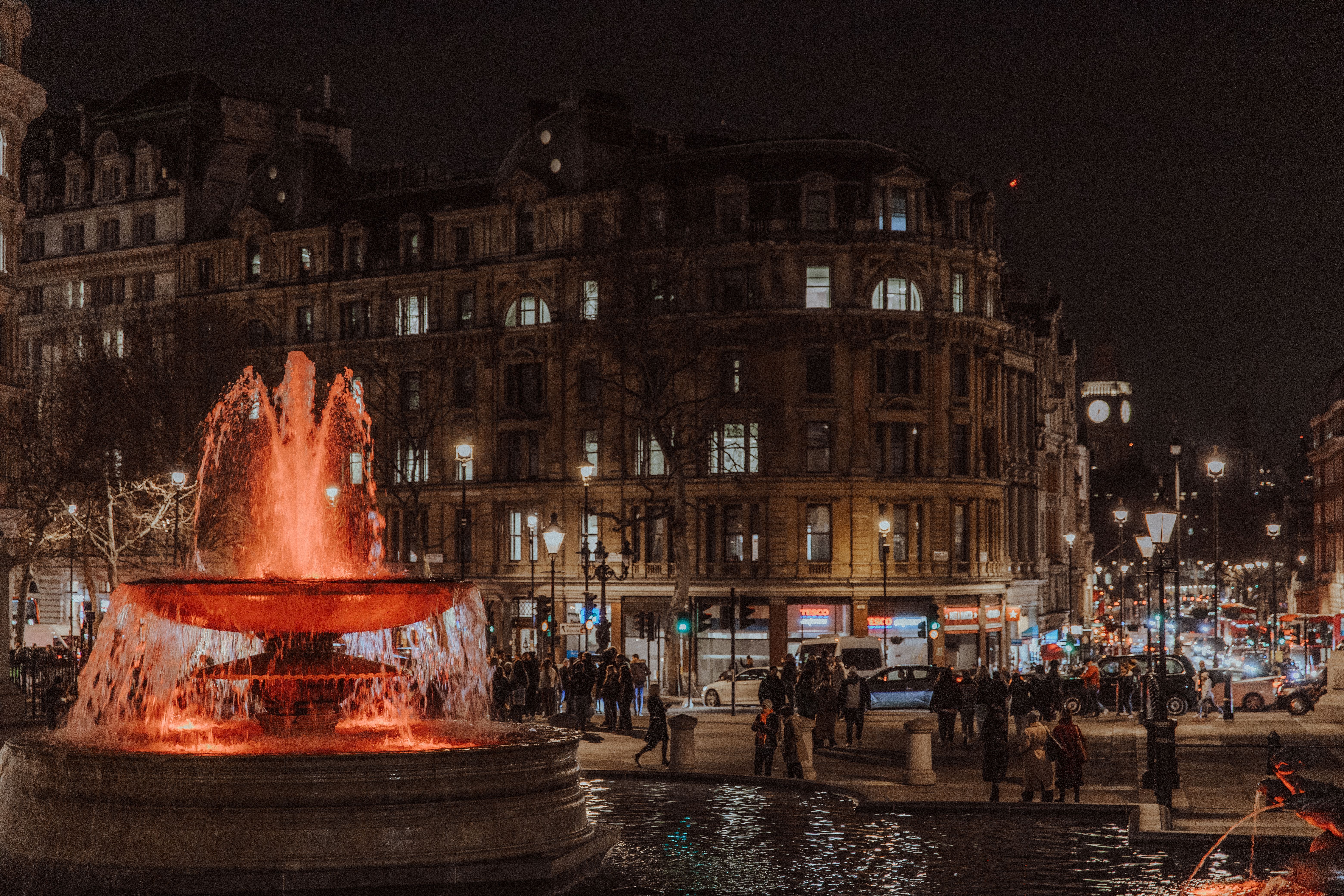 Vibrant cityscape of Trafalgar Square at night featuring the illuminated fountain and historic buildings.