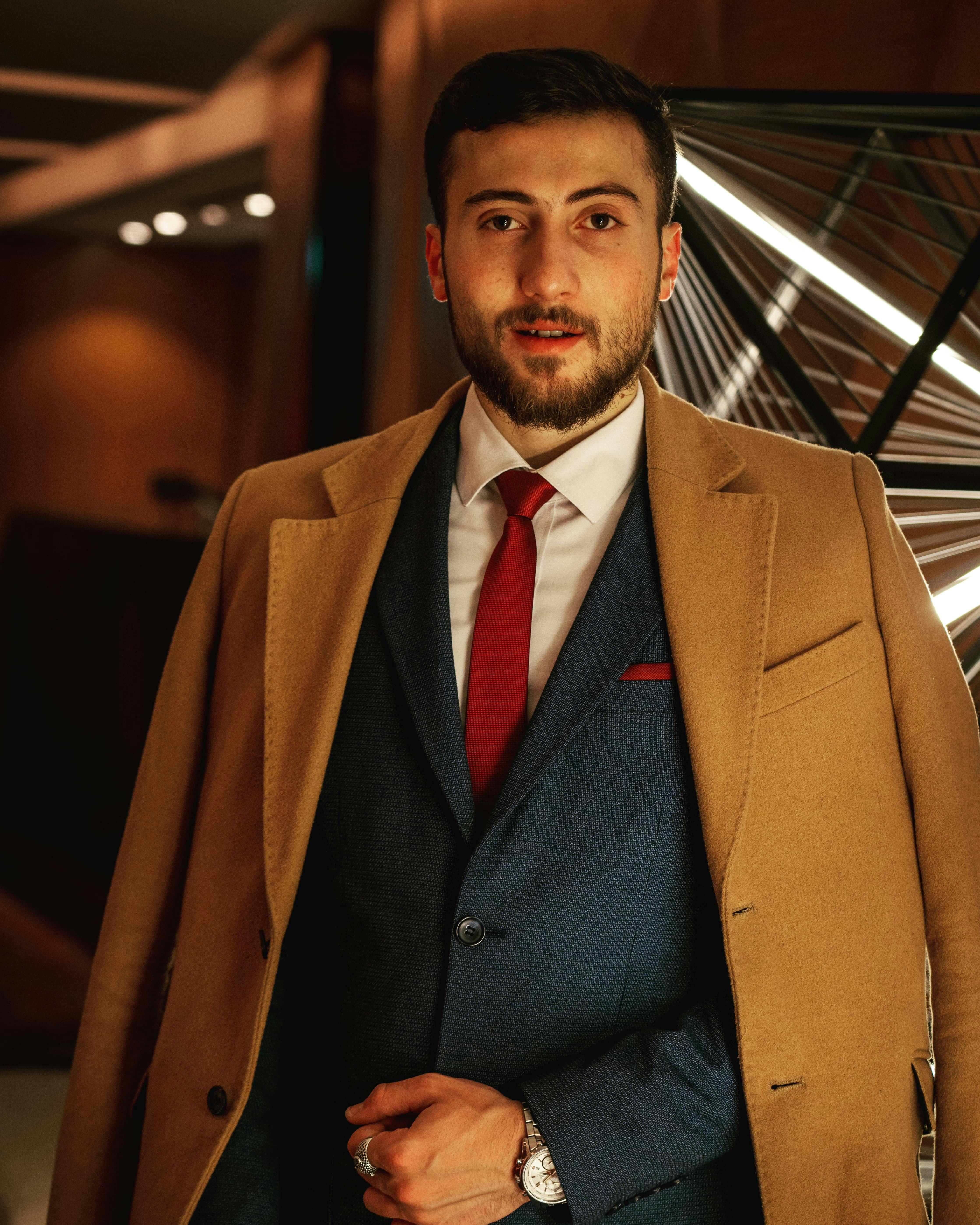 Stylish portrait of a man in a suit and coat indoors, with elegant lighting.