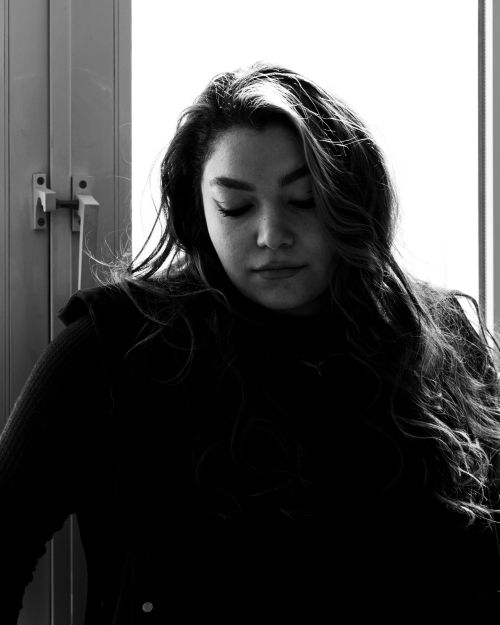 Free A pensive woman in dramatic black and white lighting, standing near a window. Stock Photo
