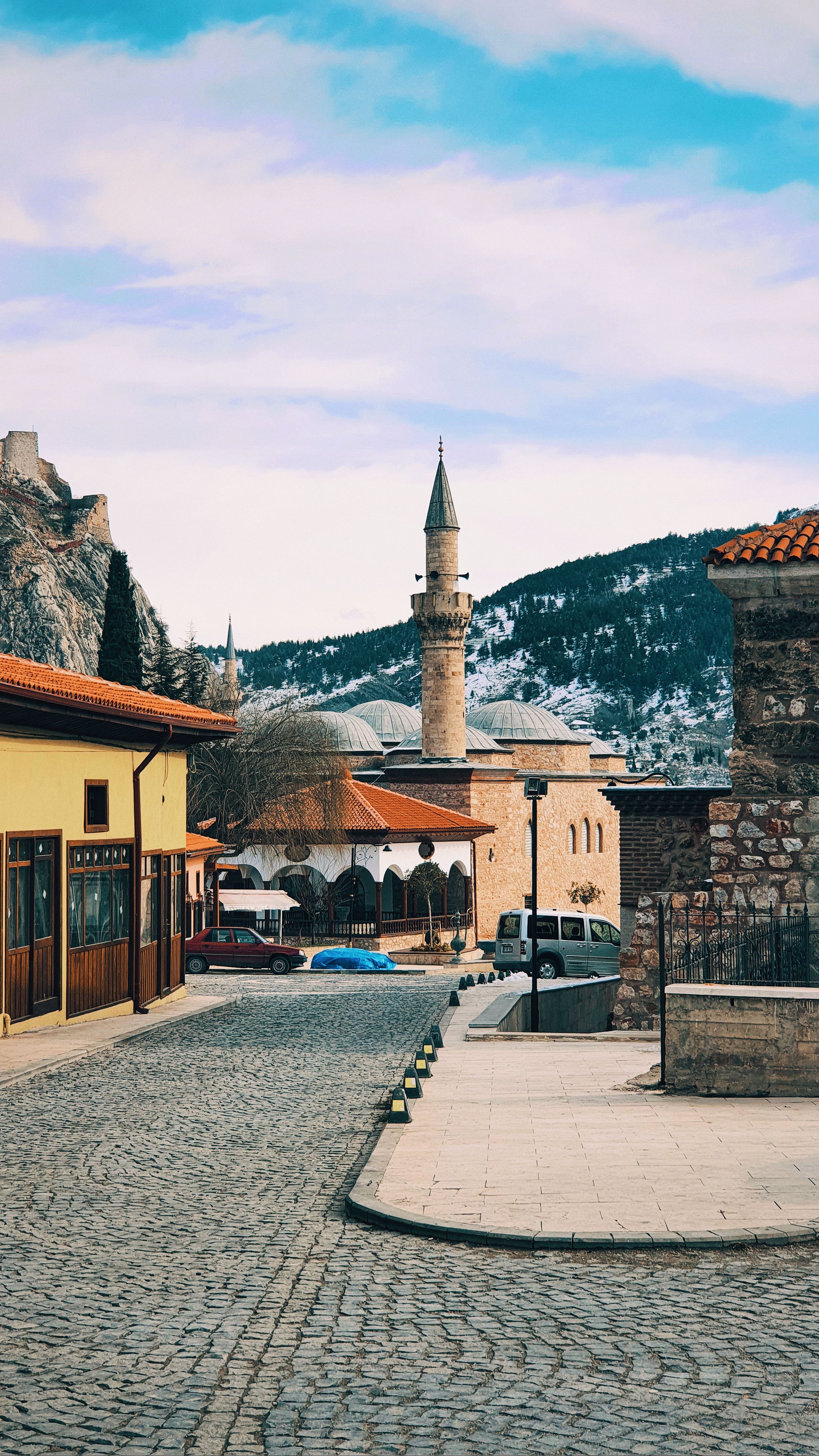 Charming street view in Tokat, Türkiye featuring a historic mosque and scenic mountain backdrop.