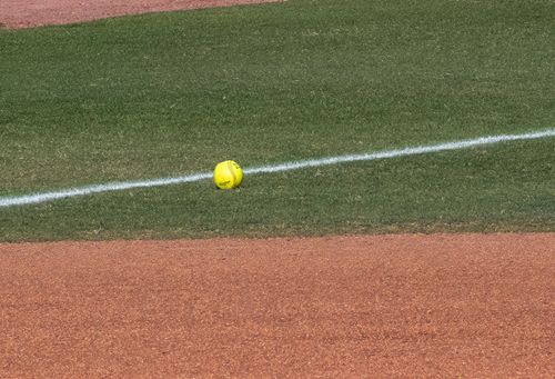 Free Close-up of a yellow softball on a baseball field with grass and red dirt. Stock Photo