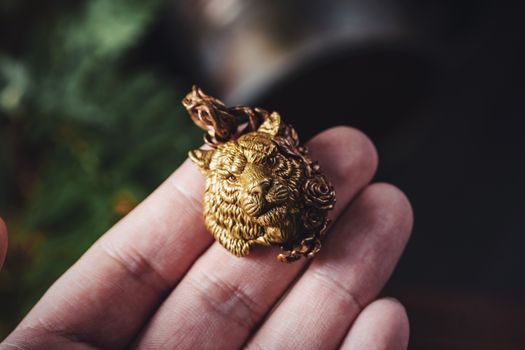 A detailed close-up of a gold lion pendant held in an adult hand, showcasing intricate design.