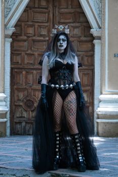 Woman in gothic Halloween costume with intricate makeup posing outdoors.
