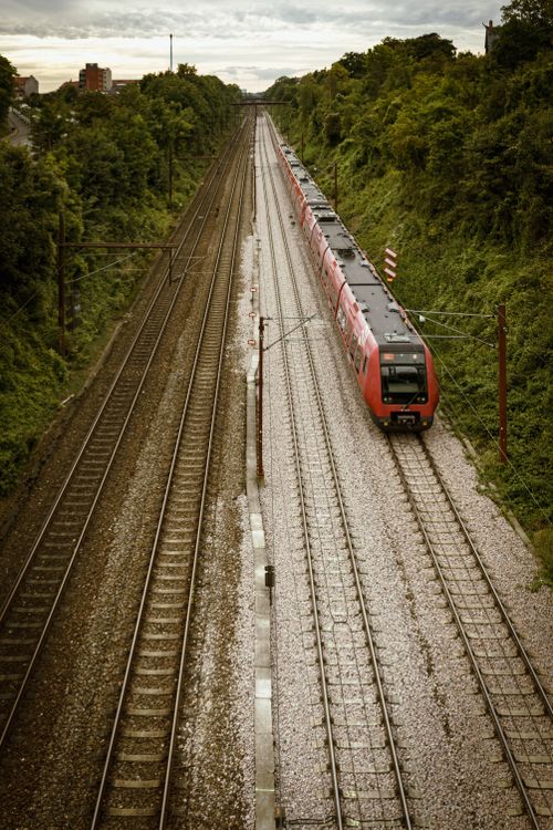 Free Aerial perspective of a red train traveling through lush greenery along railway tracks. Stock Photo