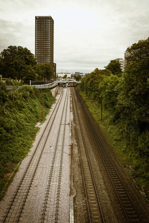 Free Aerial view of railway tracks flanked by green trees and a tall building, showcasing urban infrastructure. Stock Photo