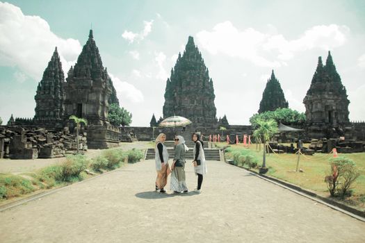 Three tourists stand with an umbrella at Prambanan Temple in Jogja, Indonesia.