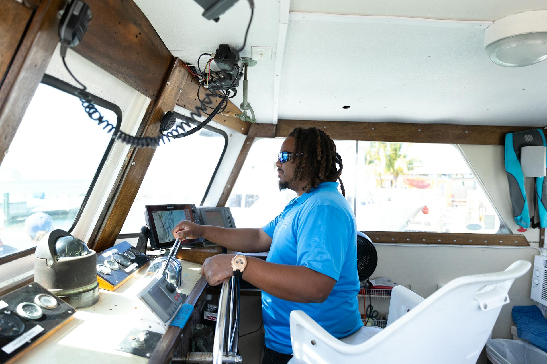 A boat captain steering a vessel, showcasing navigation equipment and a blue t-shirt inside a boat cabin.