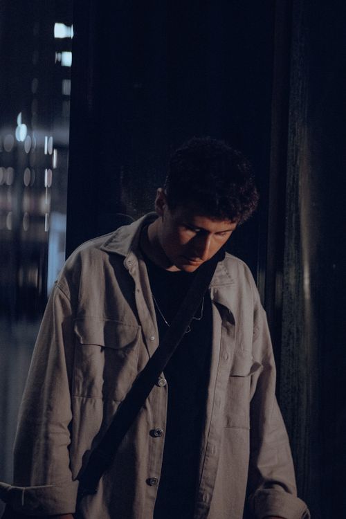 Free Young man gazing down in a dimly lit urban environment, creating a moody atmosphere. Stock Photo