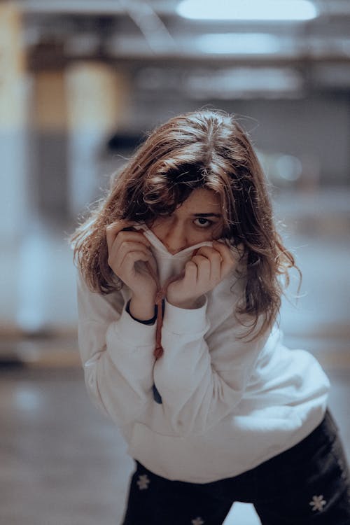 Brunette Woman Covering Mouth with White Sweatshirt