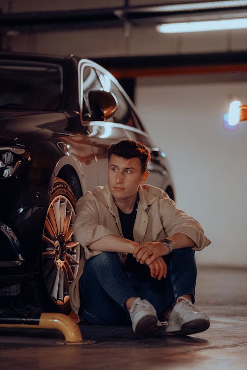 Young Man Sitting by Car in Garage Parking