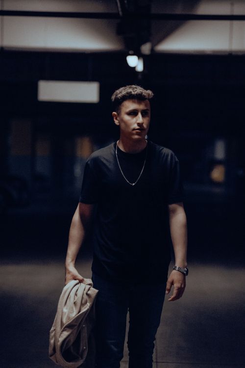 Free A young man walks confidently in a dimly lit urban setting, carrying a jacket. Stock Photo