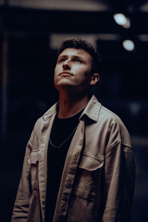 Free Young man in casual outerwear looking up thoughtfully in dimly lit urban setting. Stock Photo