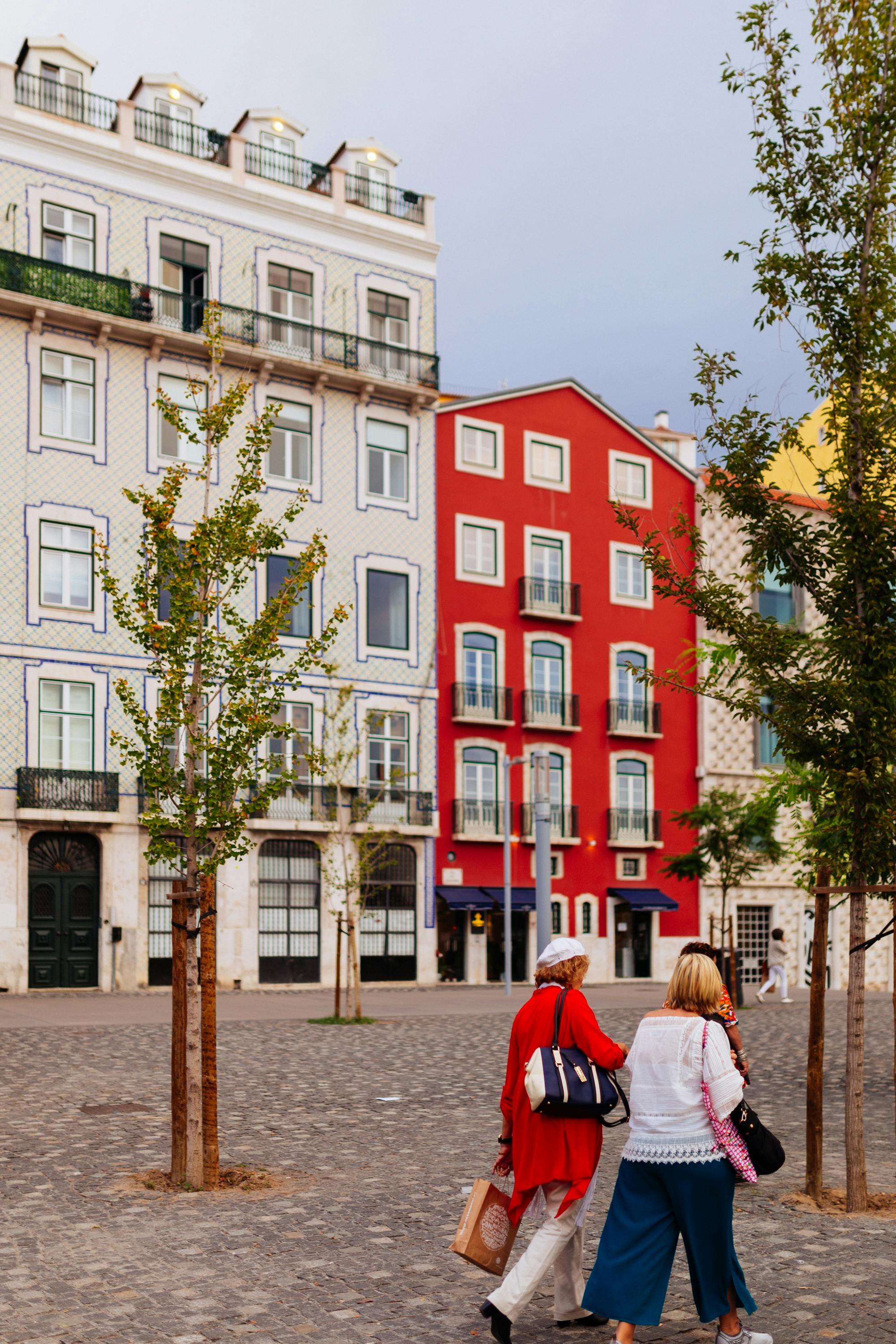 Two people walking on a cobblestone street with colorful historic buildings in the background.