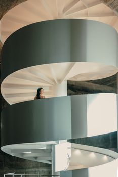 A woman stands on a modern, geometric spiral staircase in a contemporary interior setting.