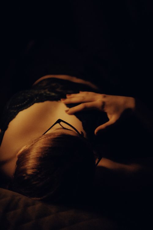 Free A mysterious woman lying in dim lighting, emphasizing eyeglasses and lingerie. Stock Photo