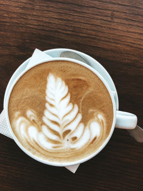 Free A beautifully crafted cappuccino with leaf latte art served on a wooden table. Perfect for coffee enthusiasts. Stock Photo